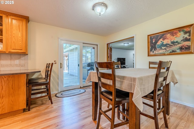 dining room with light wood-style floors, a textured ceiling, and baseboards