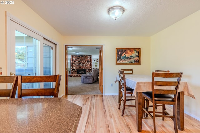 dining space featuring a fireplace, a textured ceiling, baseboards, and light wood-type flooring