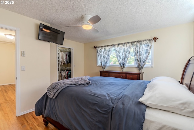 bedroom with a textured ceiling, light wood-style flooring, a ceiling fan, baseboards, and a closet