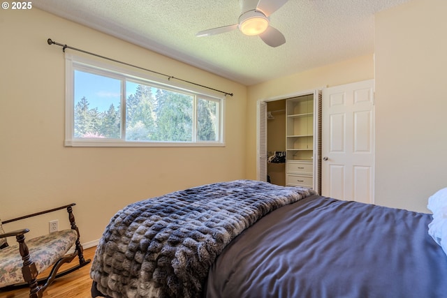 bedroom with a textured ceiling, a ceiling fan, baseboards, wood finished floors, and a closet