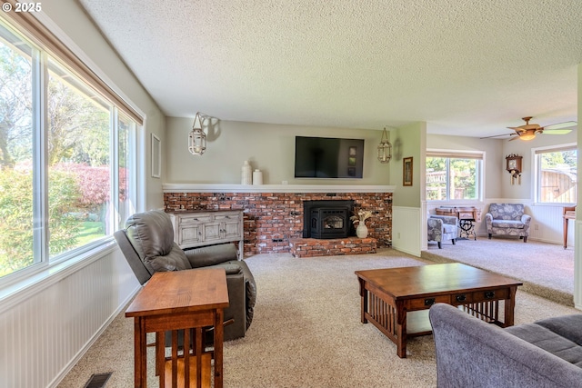 carpeted living area with a textured ceiling, visible vents, a wood stove, and a wainscoted wall