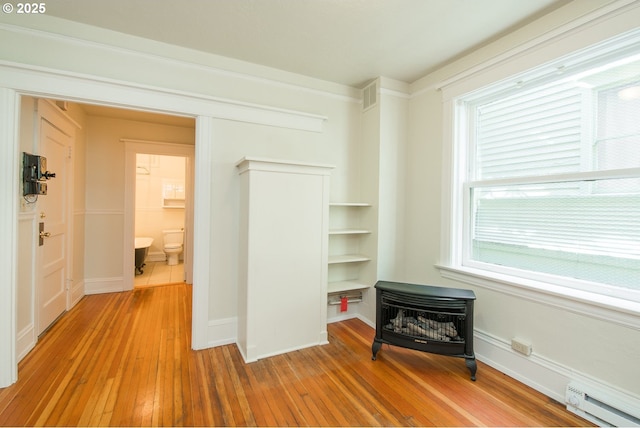 bedroom featuring a baseboard heating unit, wood-type flooring, visible vents, and baseboards