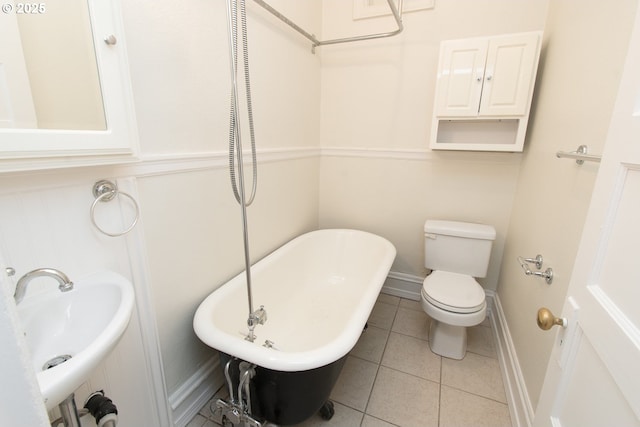 full bathroom featuring a freestanding bath, toilet, a sink, tile patterned flooring, and baseboards