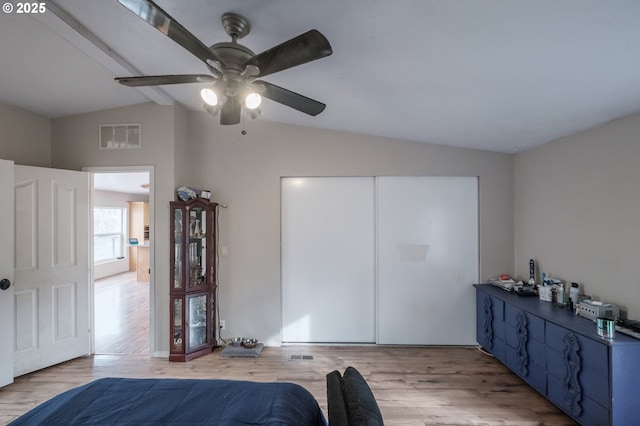 bedroom featuring visible vents, a ceiling fan, light wood-style flooring, vaulted ceiling with beams, and a closet