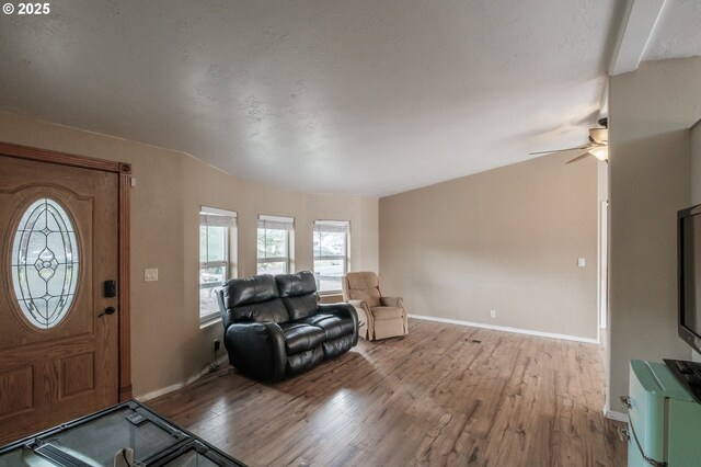 living area featuring light wood-type flooring, a textured ceiling, baseboards, and a ceiling fan