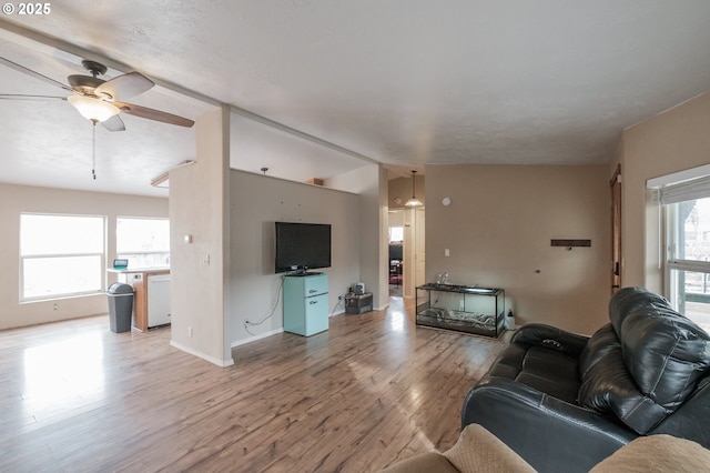 living area featuring light wood-type flooring, vaulted ceiling, ceiling fan, and baseboards