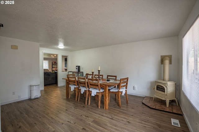 dining room featuring visible vents, wood finished floors, a wood stove, and a textured ceiling