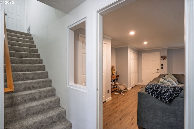 staircase with wood finished floors, crown molding, recessed lighting, and baseboards