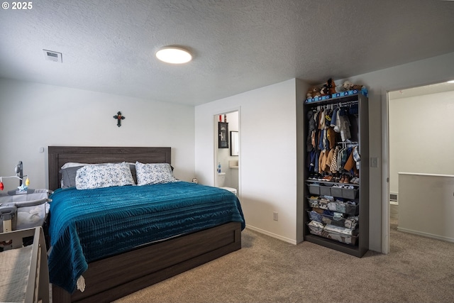 carpeted bedroom with a textured ceiling, visible vents, connected bathroom, and baseboards