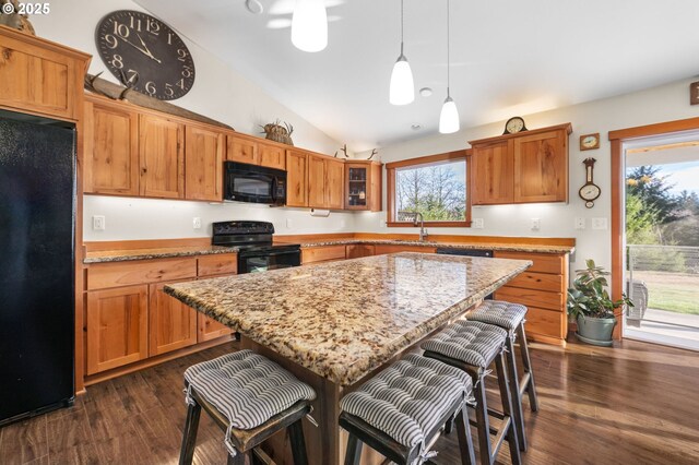 kitchen featuring decorative light fixtures, a center island, light stone counters, and black appliances