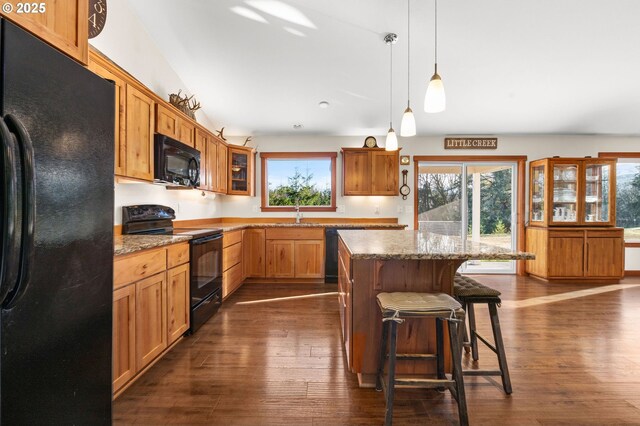 kitchen with black appliances, pendant lighting, light stone counters, and a kitchen island