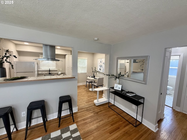9036 SE Washington St, Portland, OR 97216 - kitchen featuring freestanding refrigerator, island exhaust hood, tile counters, wood finished floors, and a textured ceiling