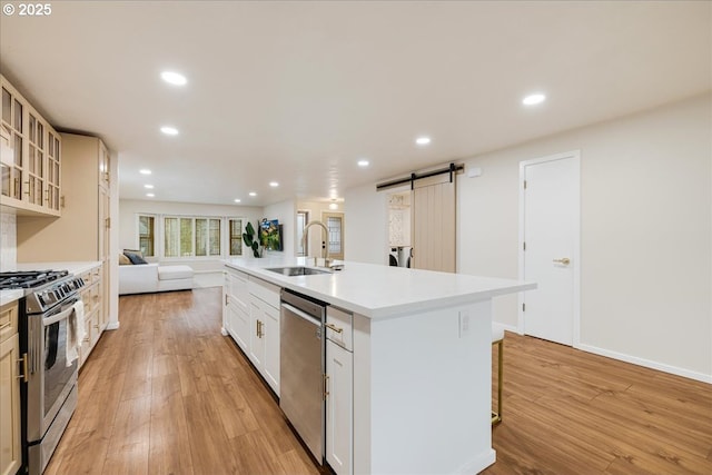 kitchen with open floor plan, a barn door, light wood-type flooring, and appliances with stainless steel finishes