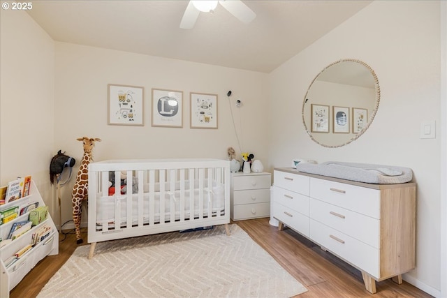 bedroom featuring light wood-style flooring, ceiling fan, and a crib