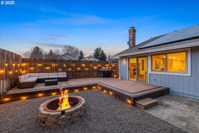 patio terrace at dusk with an outdoor living space with a fire pit, a fenced backyard, a grill, and a wooden deck