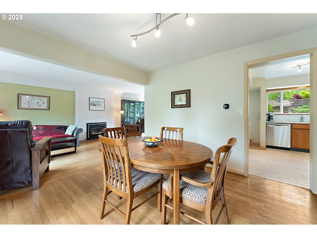 dining area featuring track lighting, baseboards, a large fireplace, and light wood-style flooring