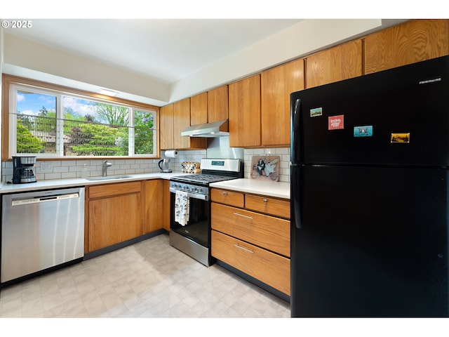 kitchen featuring decorative backsplash, light countertops, under cabinet range hood, a sink, and appliances with stainless steel finishes
