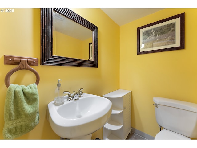 half bathroom featuring toilet, tile patterned floors, visible vents, and a sink