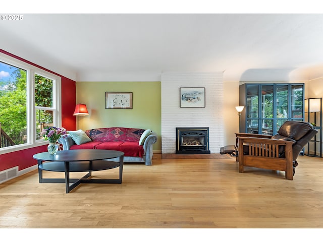 living room featuring baseboards, a brick fireplace, light wood-type flooring, and visible vents