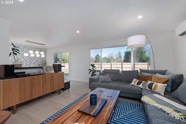 living room featuring a wall mounted AC, light hardwood / wood-style flooring, a textured ceiling, and a notable chandelier