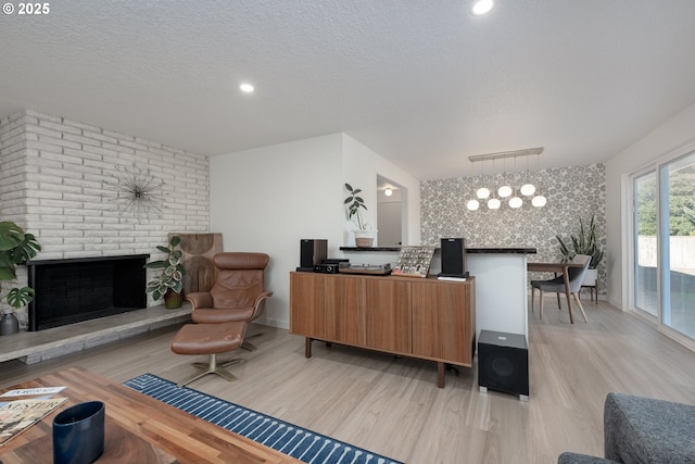 living room with light hardwood / wood-style flooring, an inviting chandelier, a textured ceiling, and a brick fireplace