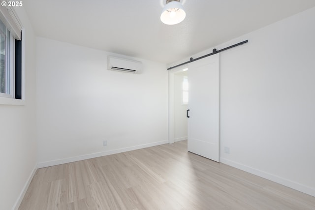 spare room with a barn door, light hardwood / wood-style flooring, and a wall mounted AC