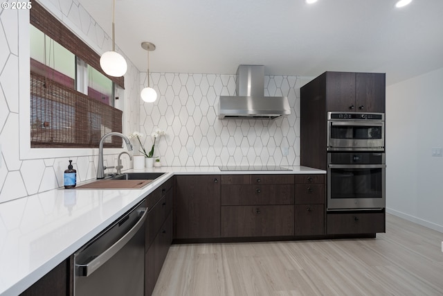 kitchen with tasteful backsplash, wall chimney exhaust hood, stainless steel appliances, sink, and hanging light fixtures