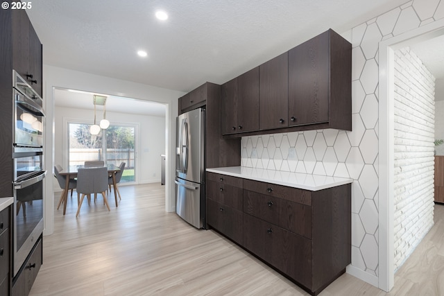 kitchen with decorative backsplash, stainless steel fridge, dark brown cabinetry, pendant lighting, and light hardwood / wood-style flooring