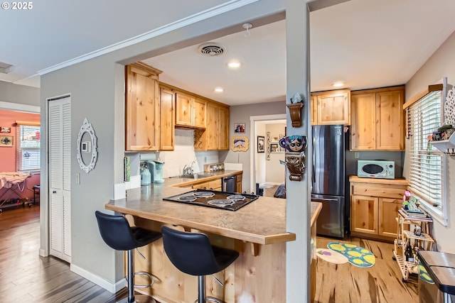 kitchen featuring white microwave, visible vents, cooktop, light wood-style flooring, and freestanding refrigerator