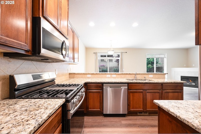 kitchen featuring stainless steel appliances, a sink, light wood-type flooring, backsplash, and light stone counters