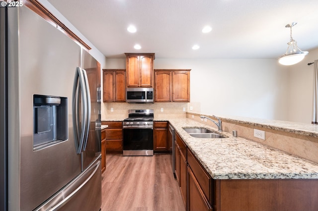 kitchen with stainless steel appliances, a sink, decorative backsplash, brown cabinets, and recessed lighting