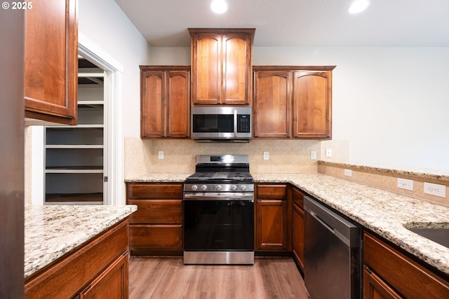 kitchen featuring stainless steel appliances, light wood finished floors, backsplash, light stone countertops, and recessed lighting