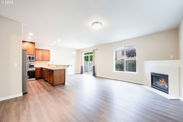 kitchen with gas stove, open floor plan, a sink, light wood-style flooring, and a peninsula