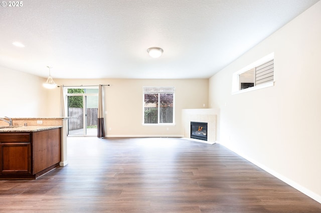 unfurnished living room featuring dark wood-style flooring, a fireplace with flush hearth, a sink, and baseboards