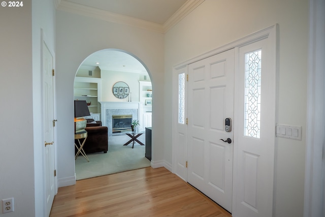 foyer entrance with light wood finished floors, a premium fireplace, baseboards, and crown molding