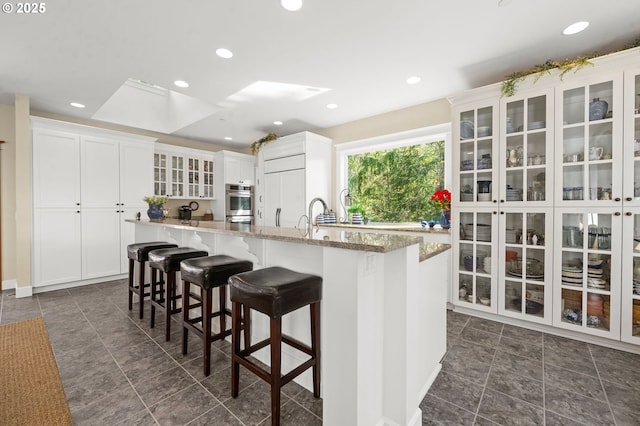 33525 Beerman Creek Ln, Seaside, OR 97138 - kitchen featuring a skylight, white cabinetry, glass insert cabinets, a kitchen bar, and a kitchen island with sink