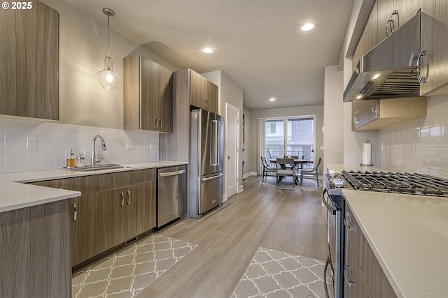 kitchen with appliances with stainless steel finishes, a sink, light countertops, light wood-style flooring, and under cabinet range hood