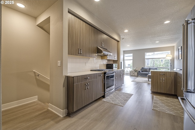 kitchen with exhaust hood, stainless steel appliances, a textured ceiling, and light wood finished floors
