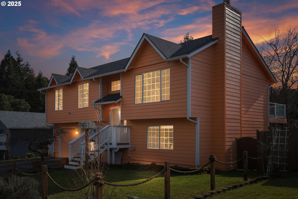 back house at dusk featuring a garage and a lawn