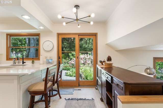 doorway to outside with a sink, a chandelier, ornamental molding, light tile patterned flooring, and healthy amount of natural light
