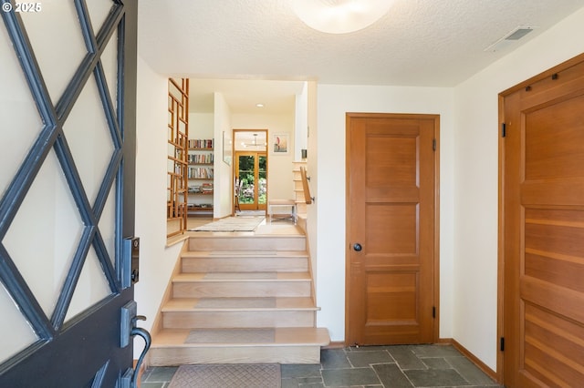entrance foyer featuring dark stone finish flooring, a textured ceiling, stairs, and baseboards