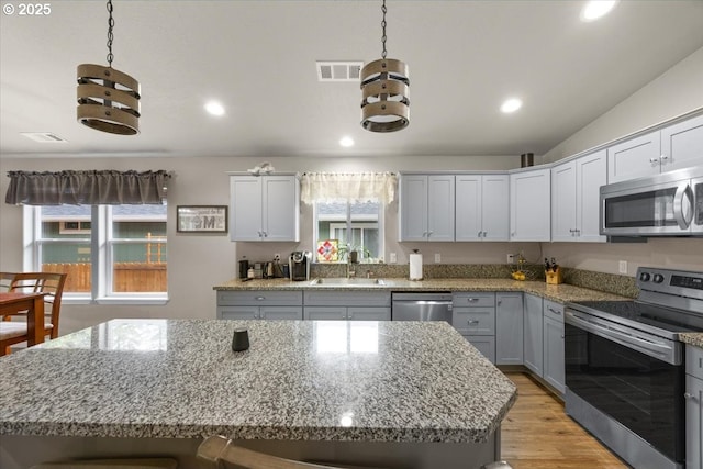kitchen featuring stainless steel appliances, a sink, a kitchen island, gray cabinets, and light wood finished floors
