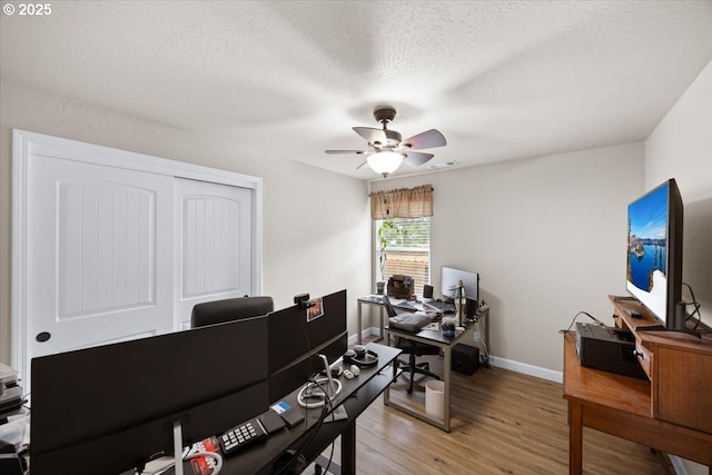 office featuring a ceiling fan, light wood-style flooring, baseboards, and a textured ceiling