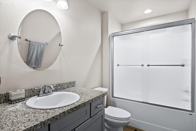 bathroom with toilet, enclosed tub / shower combo, vanity, a textured wall, and recessed lighting