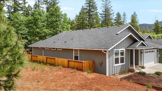 rear view of property featuring roof with shingles, fence, driveway, and an attached garage