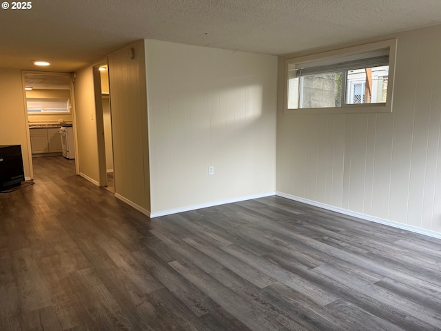 spare room with a textured ceiling, dark wood-style flooring, washing machine and dryer, and baseboards