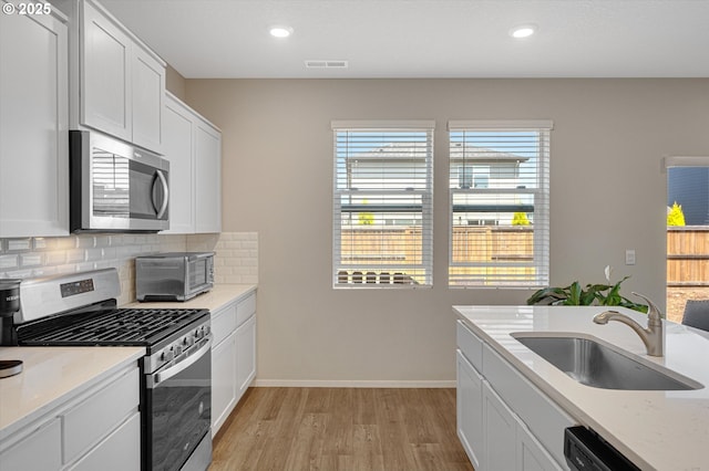 4829 Surveyor Ave, Salem, OR 97305 - kitchen featuring appliances with stainless steel finishes, a sink, light wood finished floors, decorative backsplash, and white cabinets
