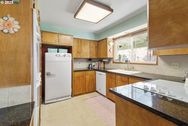 kitchen featuring sink, white appliances, kitchen peninsula, decorative backsplash, and dark stone counters