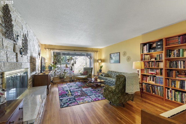 living room with hardwood / wood-style flooring, a stone fireplace, and a textured ceiling