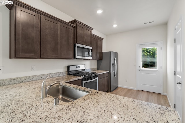 1712 W 12th St, La Center, WA 98629 - kitchen featuring stainless steel appliances, a sink, light wood finished floors, dark brown cabinets, and light stone counters